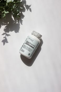 Biotin supplement bottle for hair health on a white surface with natural light and plant shadows.