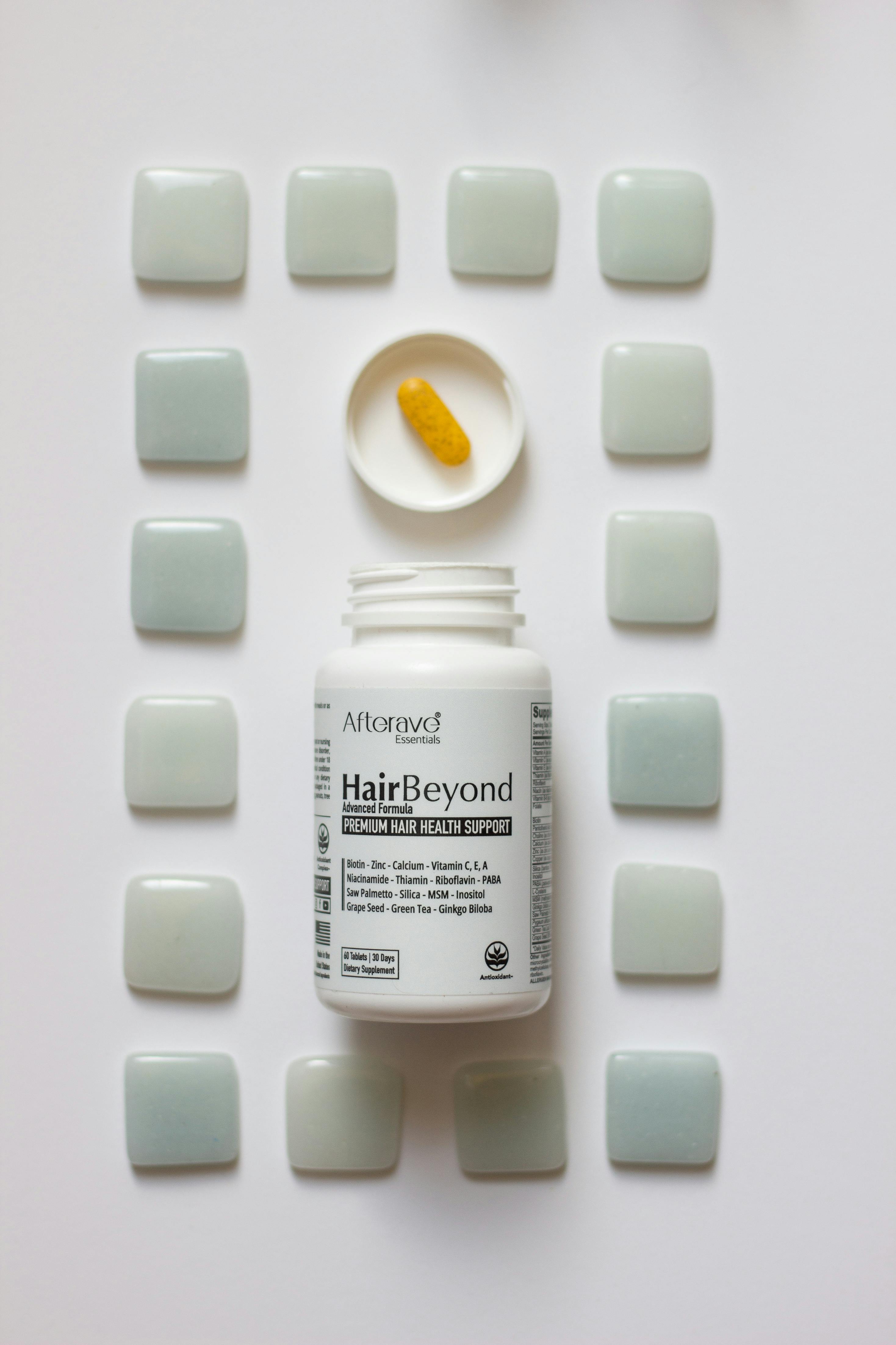 Biotin hair health supplement bottle and orange softgel surrounded by geometric tile pattern.