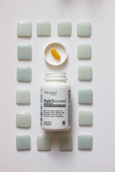 Biotin hair health supplement bottle and orange softgel surrounded by geometric tile pattern.