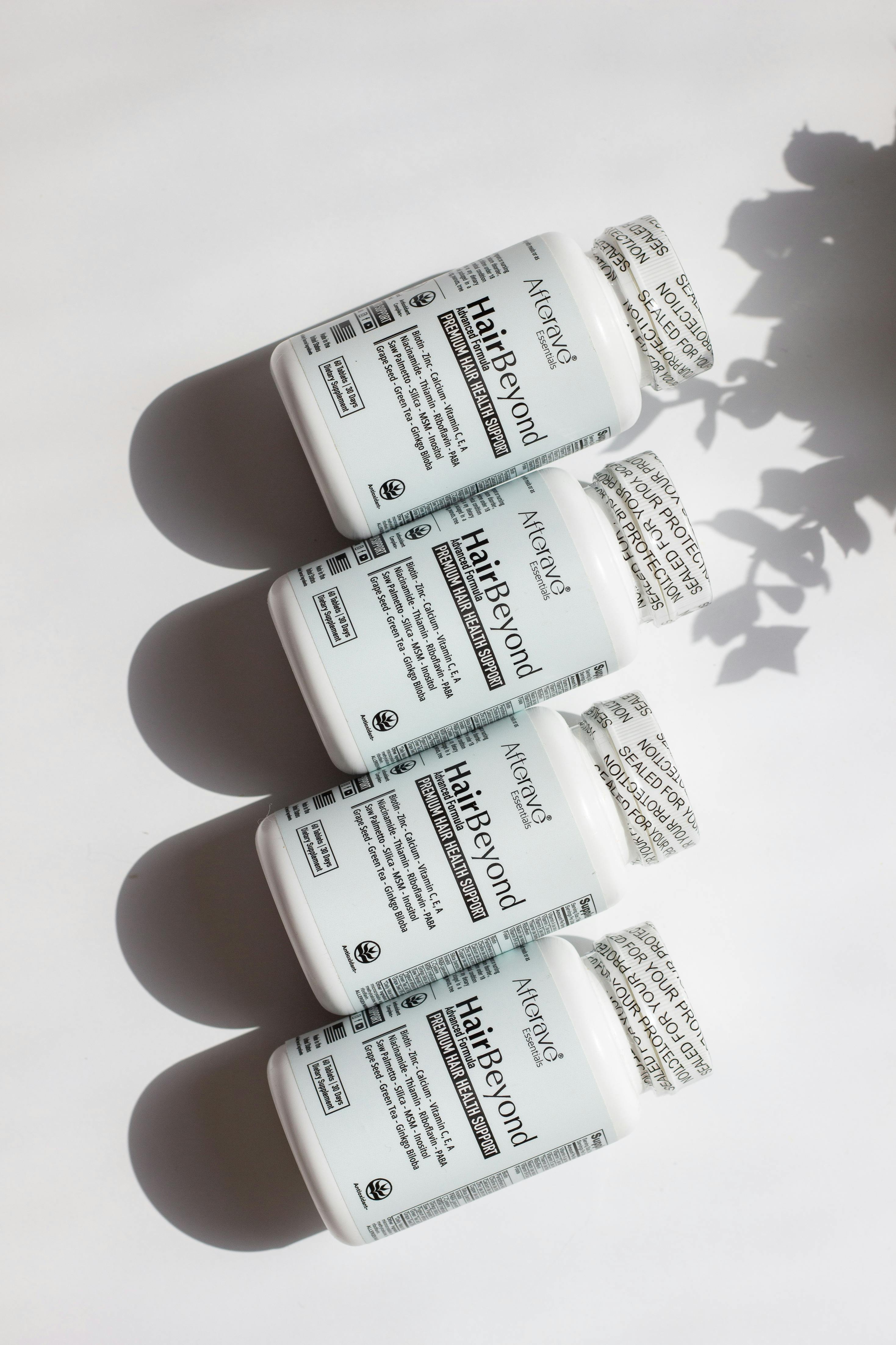 Four bottles of hair and nail vitamins on a white surface, casting shadows in bright daylight.