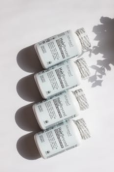 Four bottles of hair and nail vitamins on a white surface, casting shadows in bright daylight.