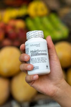 A hand holding a bottle of Afterave HairBeyond supplement with fruits in the background.
