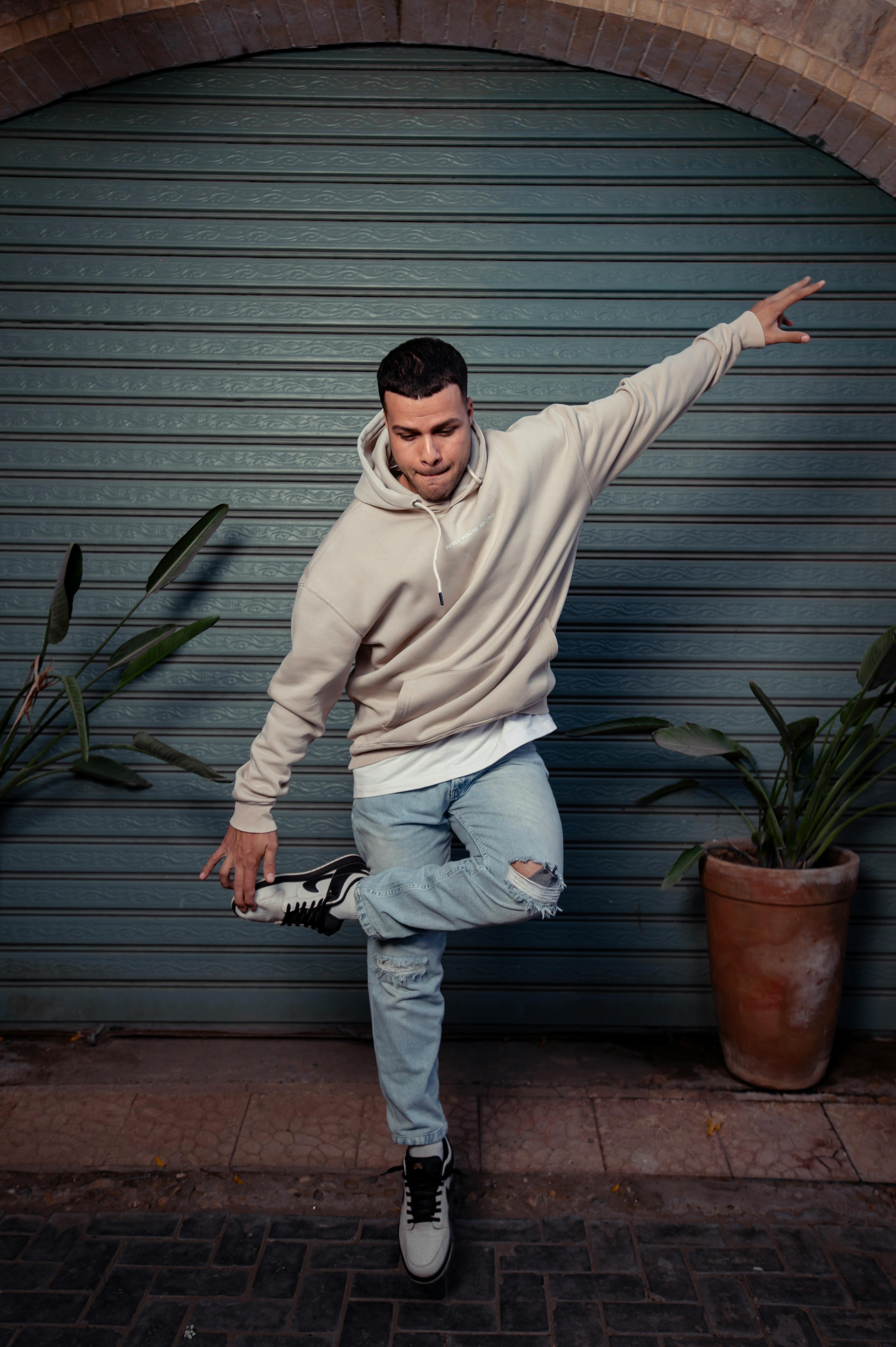 Young adult in a hoodie striking a dynamic pose outdoors by a shuttered door.