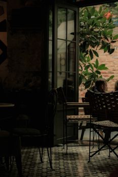 Dimly lit cafe interior with view of outdoor seating and green foliage.