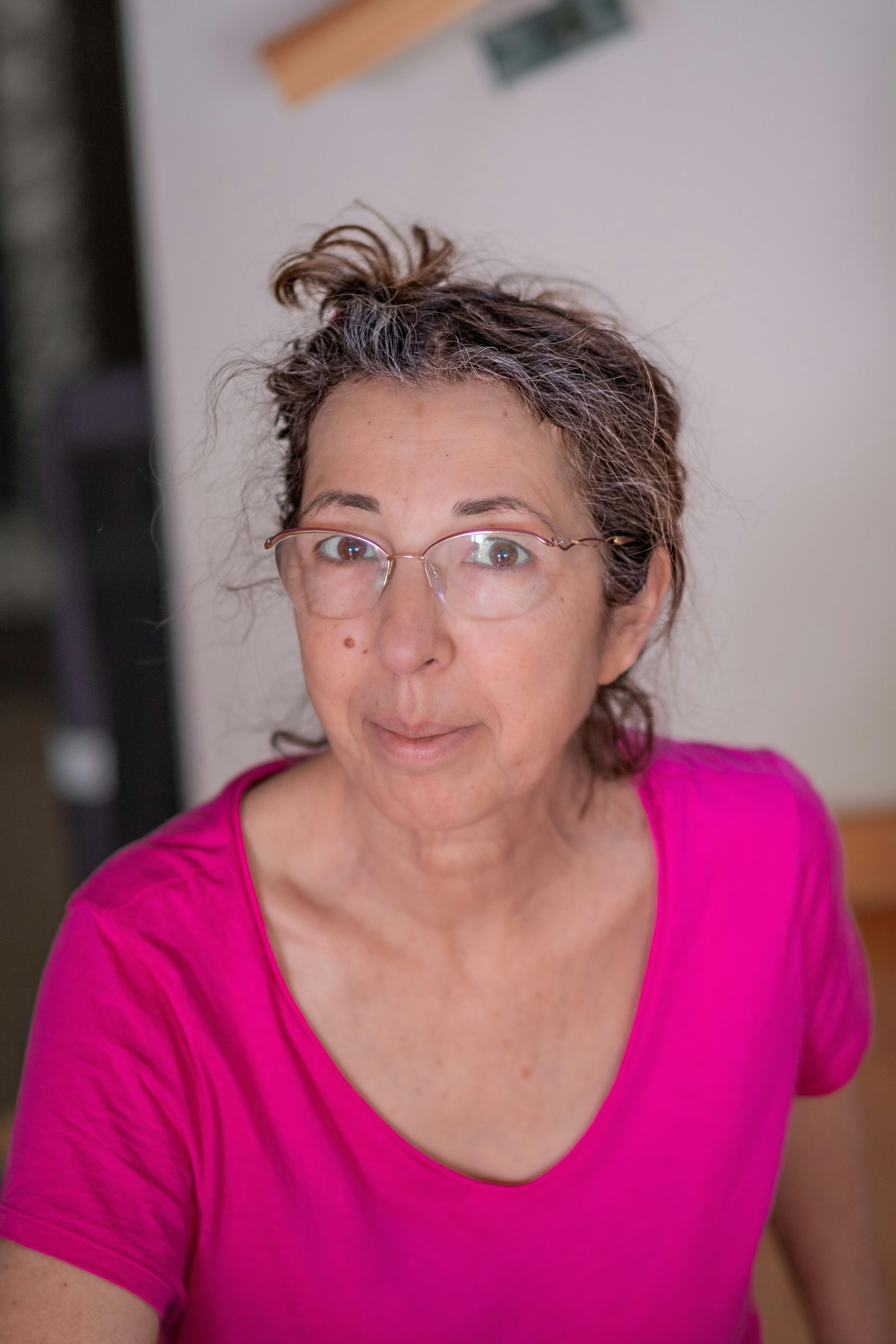 Casual portrait of a woman wearing glasses and a bright pink top, looking at the camera.