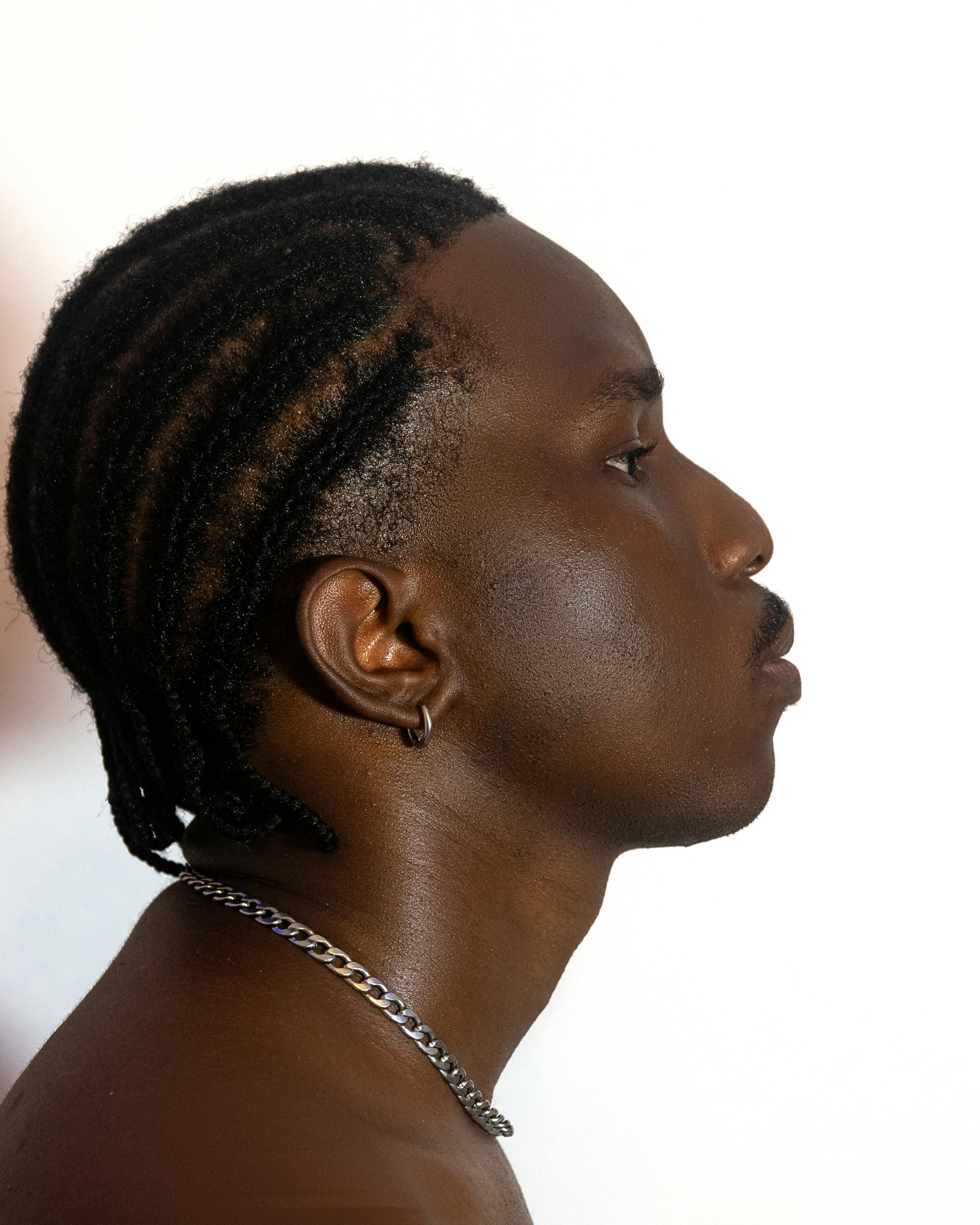 Side profile portrait of an adult man with braided hair and earring against a white background.