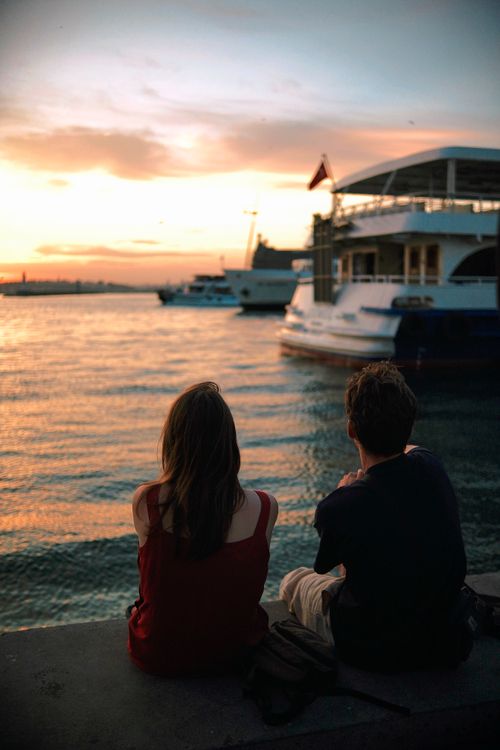 Free Couple enjoying a sunset by the waterfront, seated near a ferry. Stock Photo