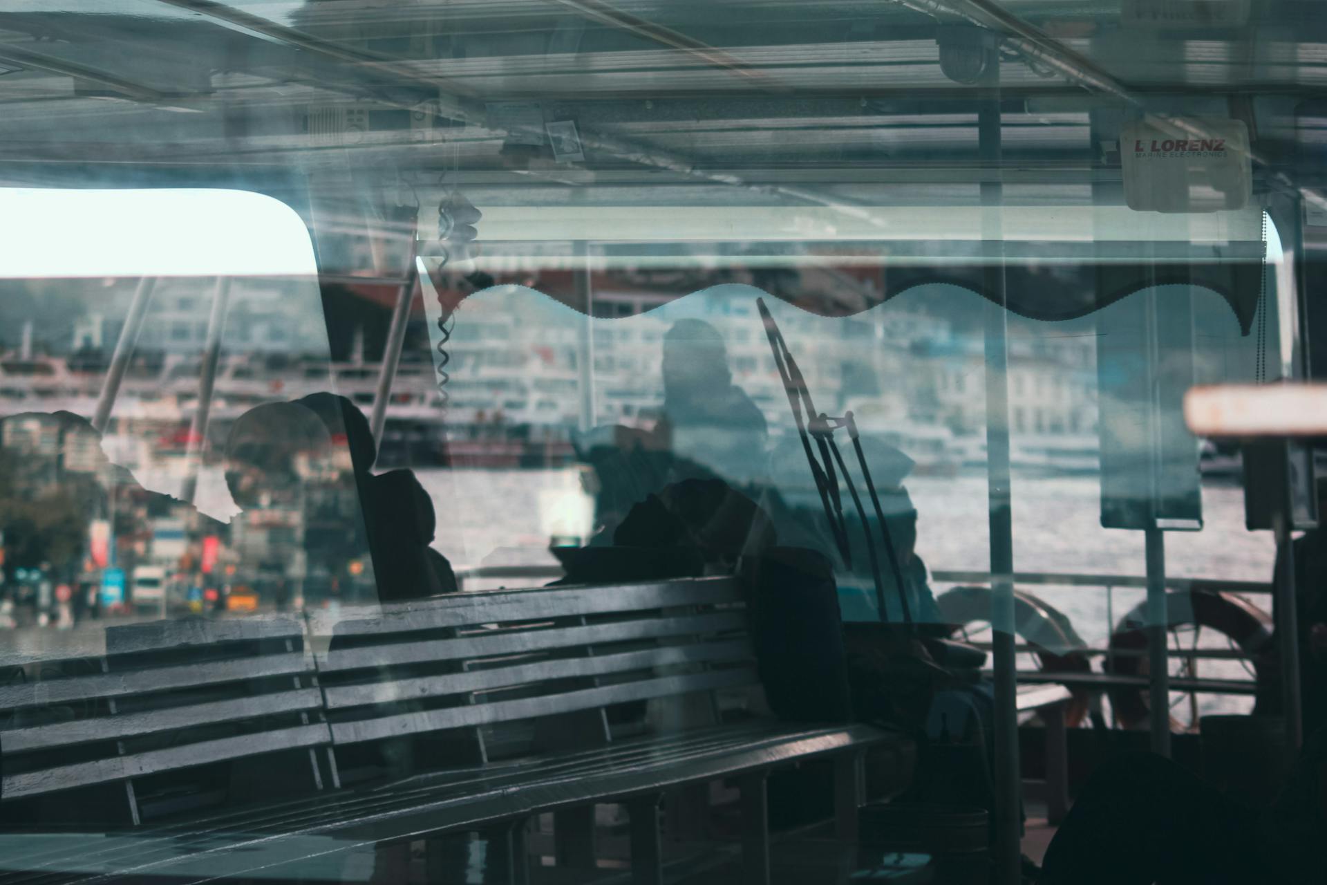 Silhouetted passengers reflected on a ferry window with a cityscape view.