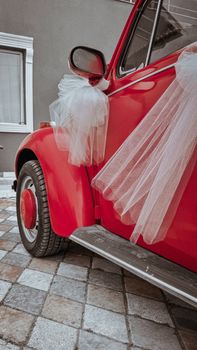 Close-up of a red vintage car with white tulle decorations for a wedding event.