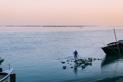 Free A fisherman stands on rocks in the Brahmaputra River during sunset in Chilmari, Bangladesh. Stock Photo