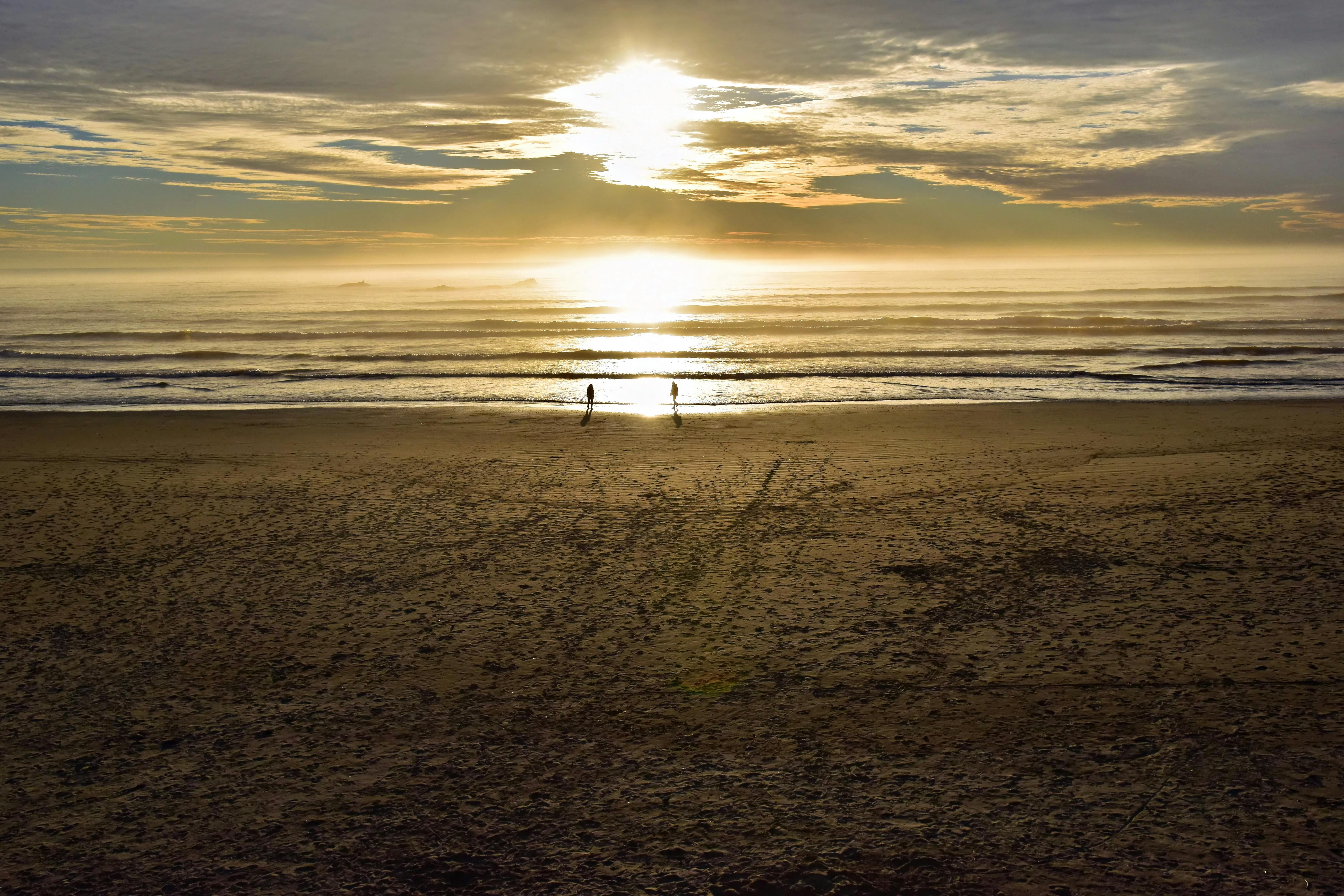 Peaceful sunset scene at Kalaloch Beach, Washington, with silhouette of two people walking along the shore.