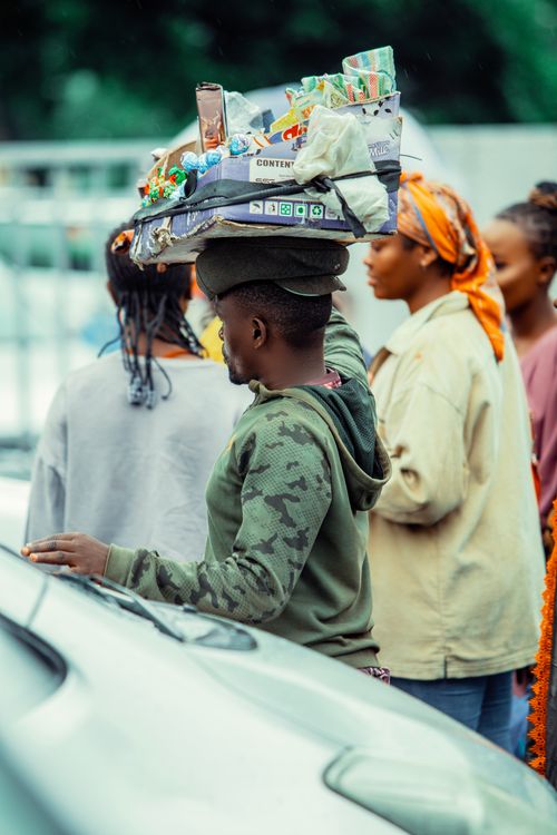 Free A street vendor skillfully balances a variety of products on his head while walking through a busy city street. Stock Photo
