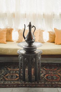 Beautiful Tunisian interior with ornate metal teapot on carved wooden table, rich textiles.
