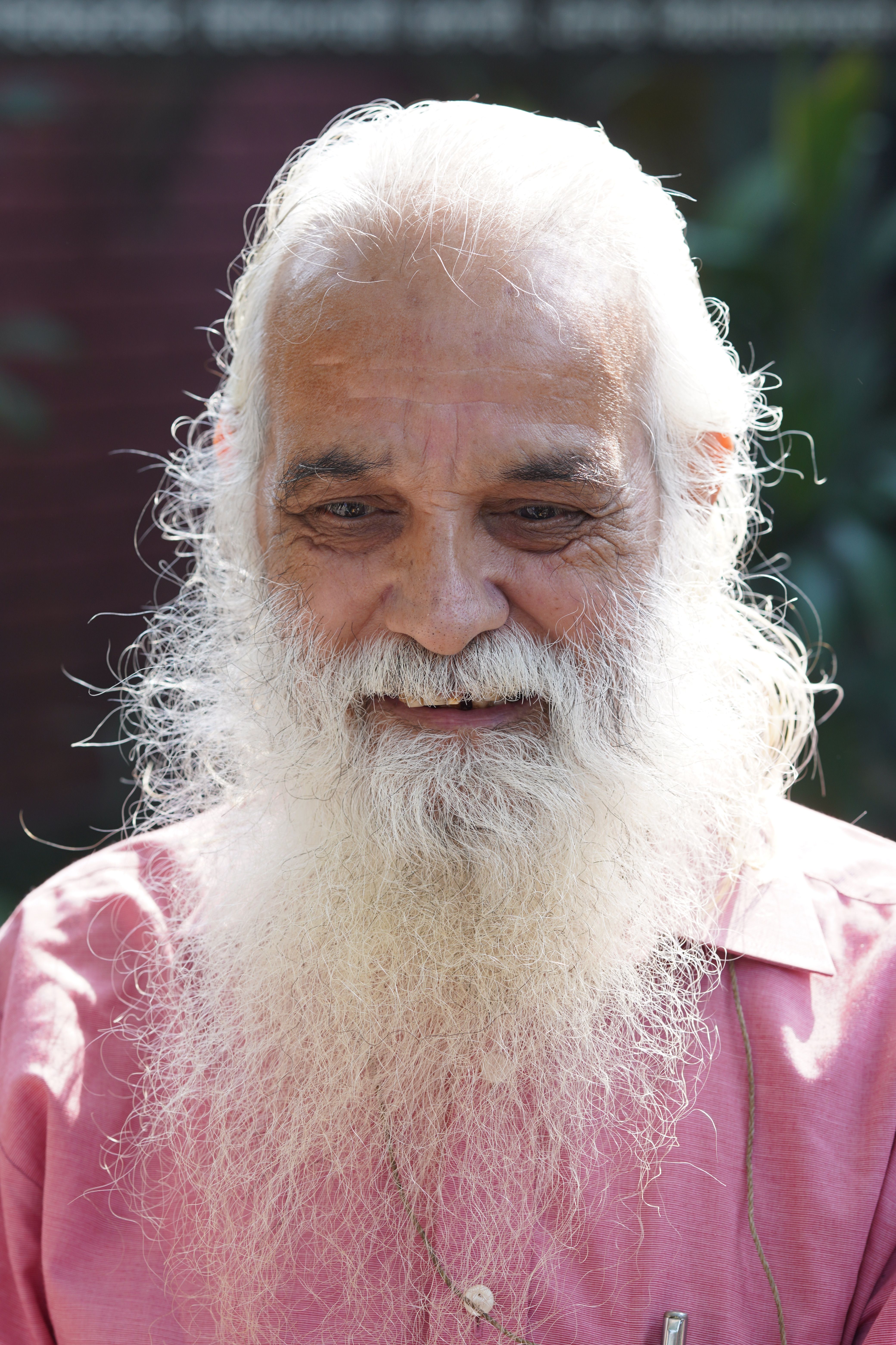 Portrait of a senior man with a white beard smiling under sunlight outdoors.