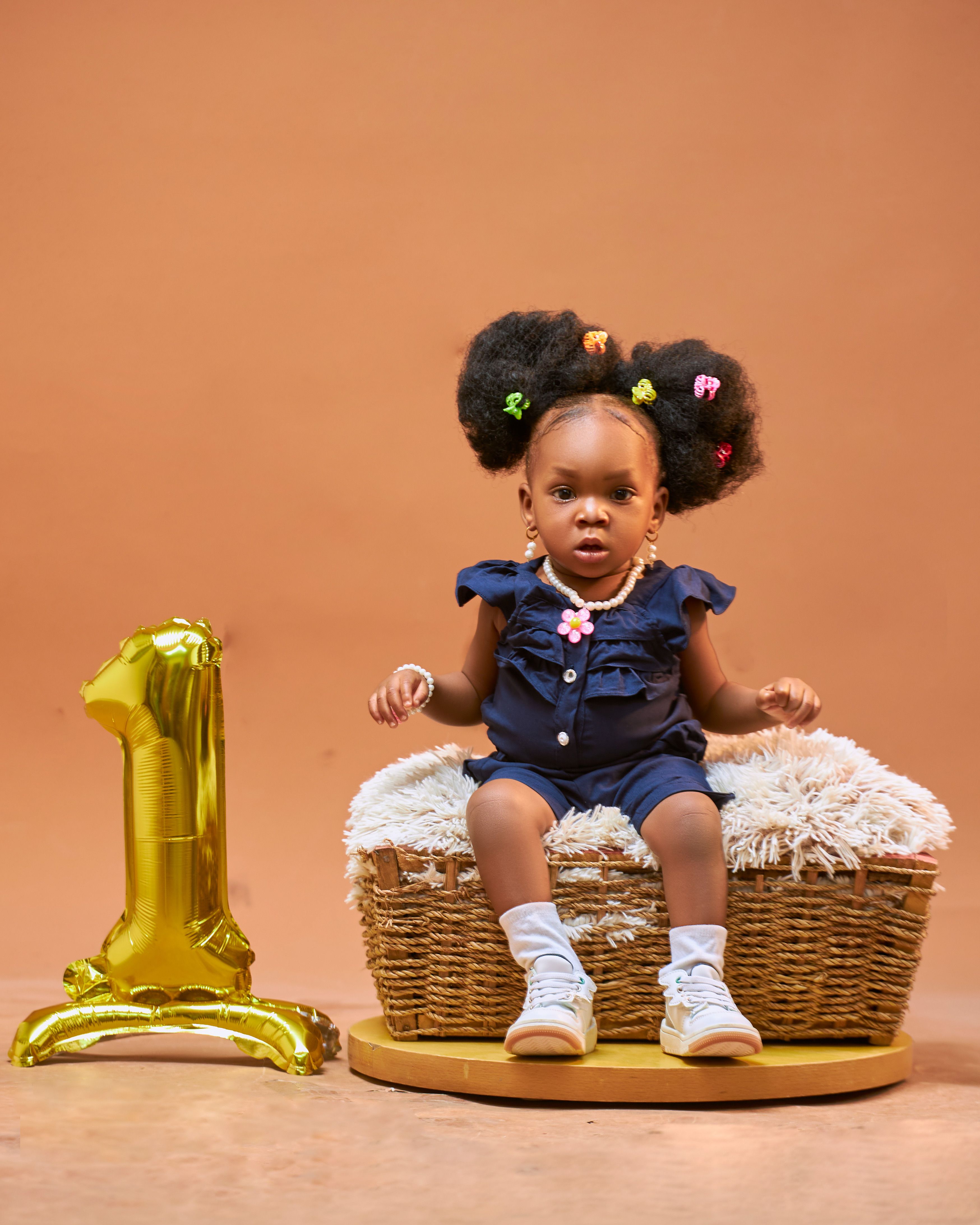 Cute infant girl celebrates first birthday with balloon and stylish outfit.