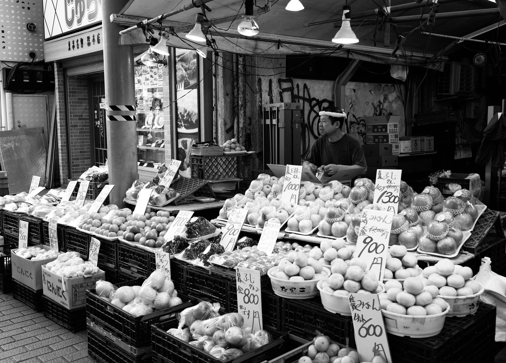Black and white image of a traditional Japanese street market with various fruits and a vendor.