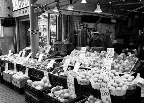 Free Black and white image of a traditional Japanese street market with various fruits and a vendor. Stock Photo