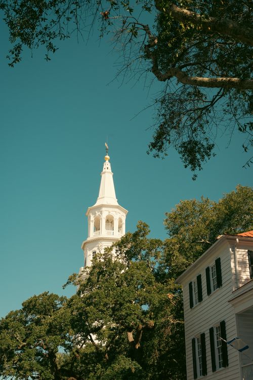 Free A classic white church steeple amidst trees under a clear blue sky in a historic setting. Stock Photo