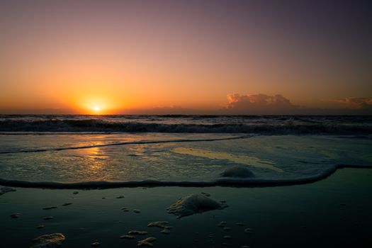Captivating view of the sun setting over ocean waves, casting a warm glow on a tranquil beach.