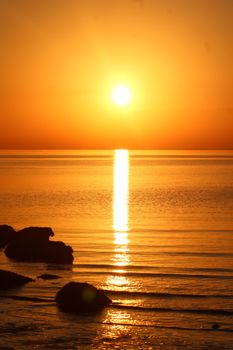 Stunning sunset over the ocean with a vibrant golden reflection and silhouetted rocks.