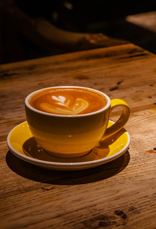 Free Cozy cappuccino with latte art in a yellow cup, set on a rustic wooden table. Stock Photo