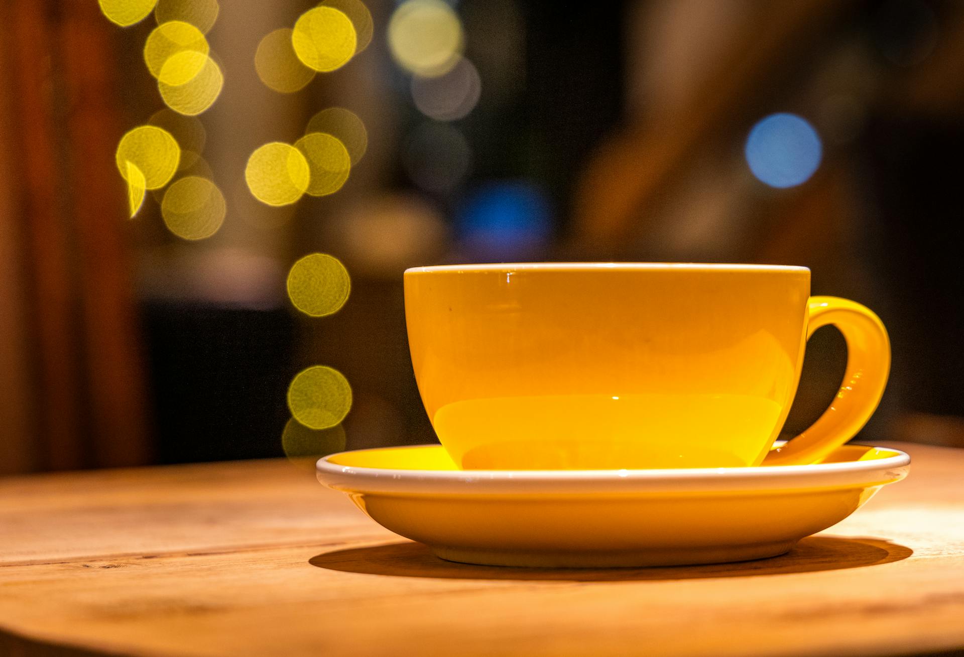 Bright yellow coffee cup on rustic table with beautiful bokeh lights in the background.