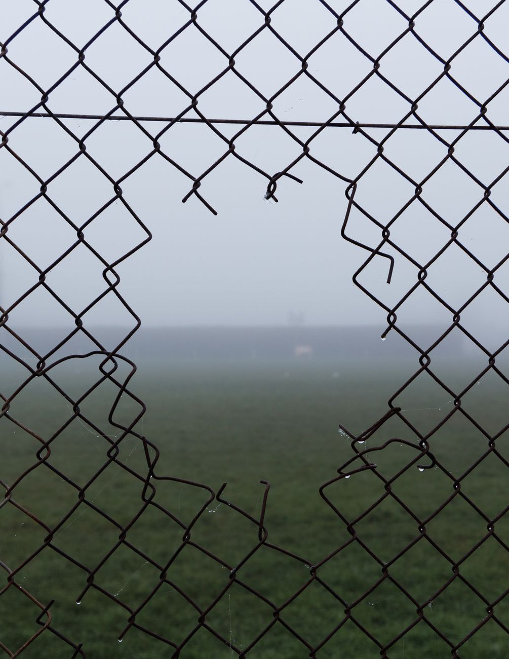 A broken chain link fence with a foggy background creating a mysterious atmosphere.