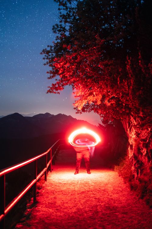 Free A person creates vibrant red light trails on a night hike in Bavaria, Germany, under a starry sky with mountains in the background. Stock Photo