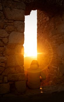 A traveler enjoys a serene sunset view through an ancient stone archway in Spain.