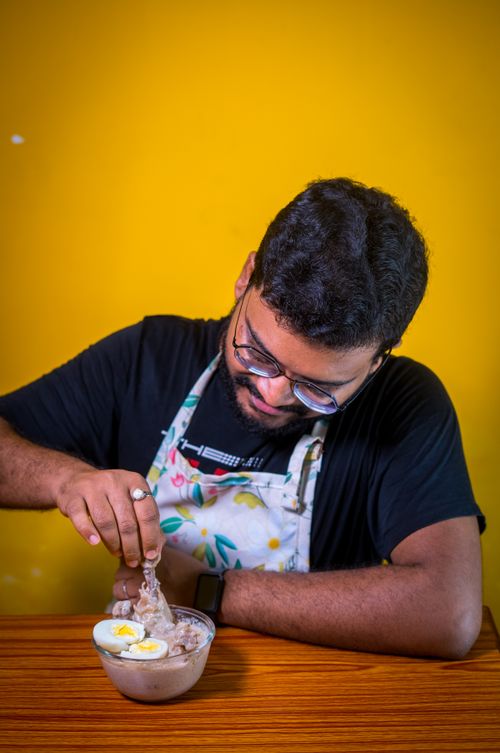 Free Man in apron preparing an egg dish against a vibrant yellow backdrop. Stock Photo