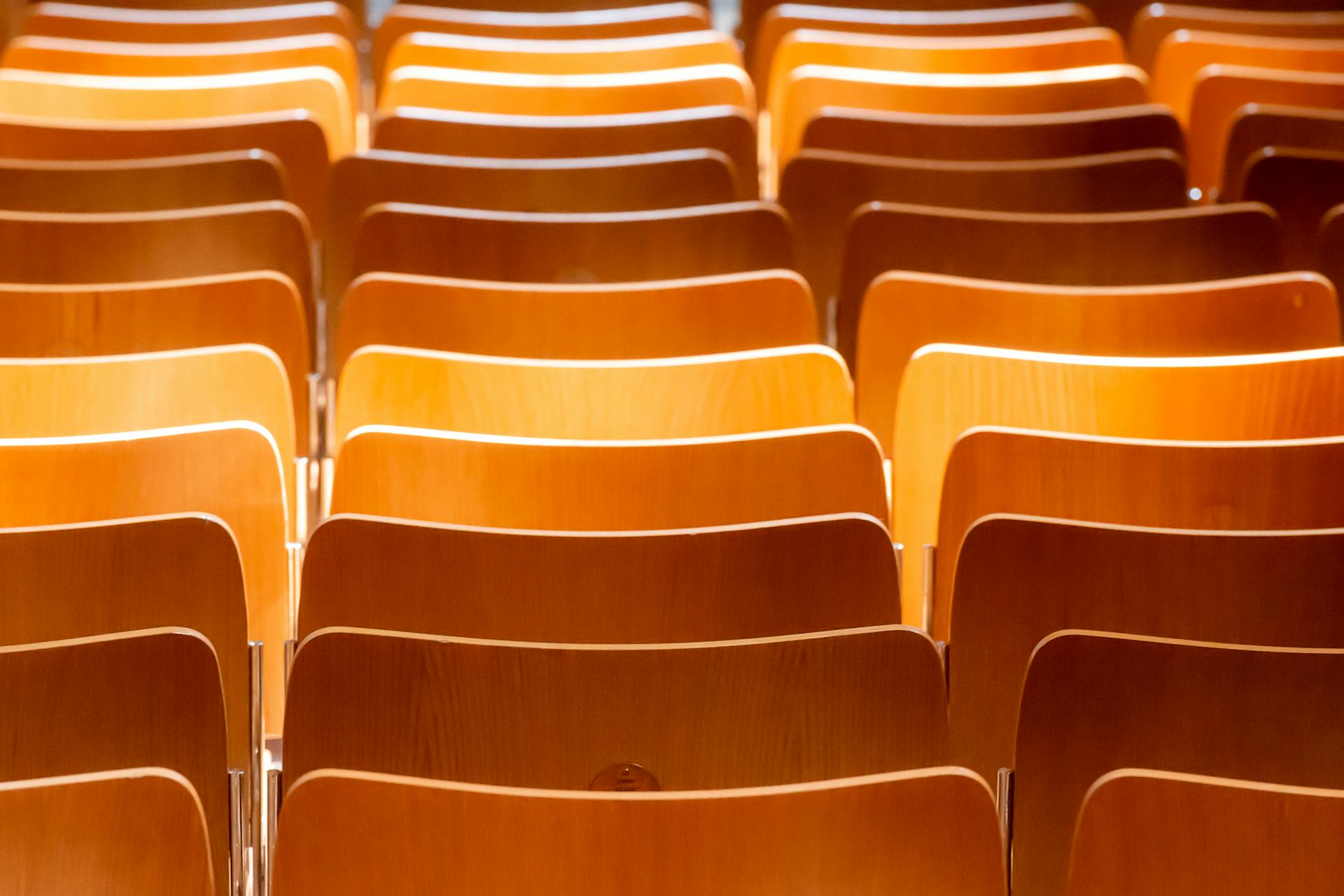 Rows of wooden chairs arranged in an indoor setting, softly lit and awaiting use.