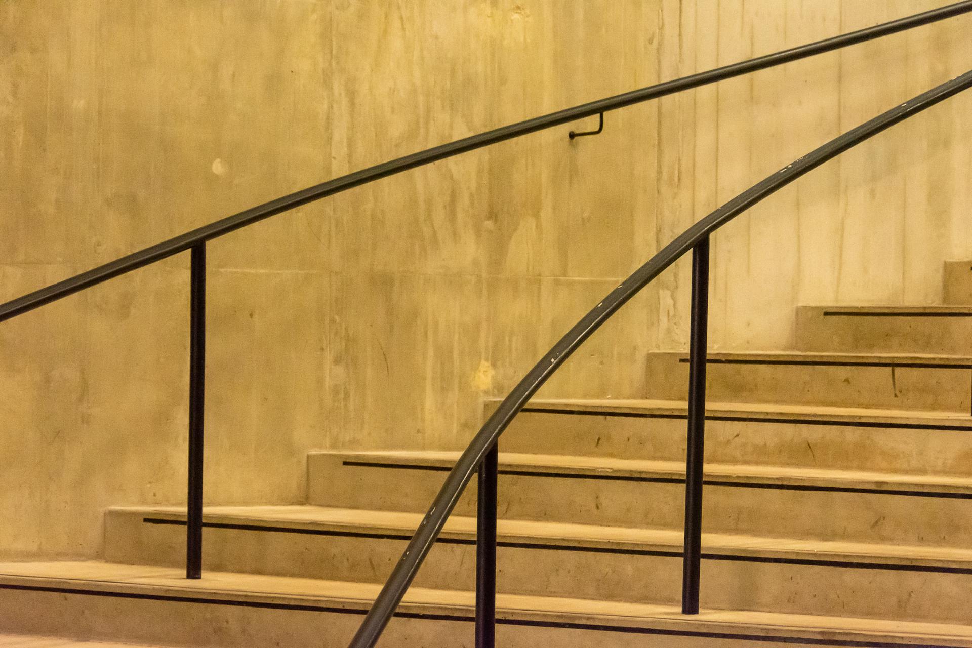 Concrete staircase with sleek metal railings in an indoor setting, showcasing minimalist design.