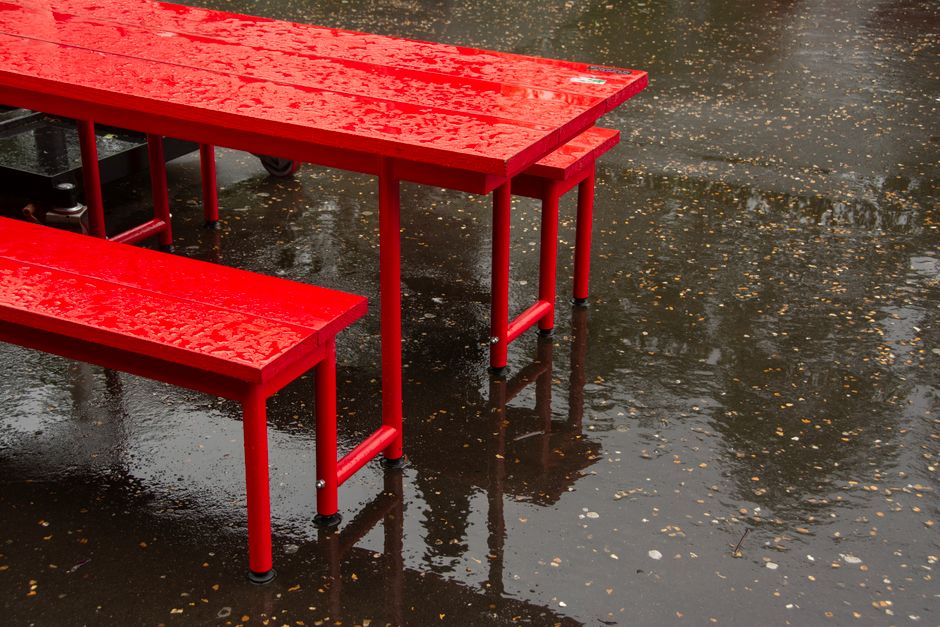 Bright red table and bench set on wet asphalt with rain droplets.