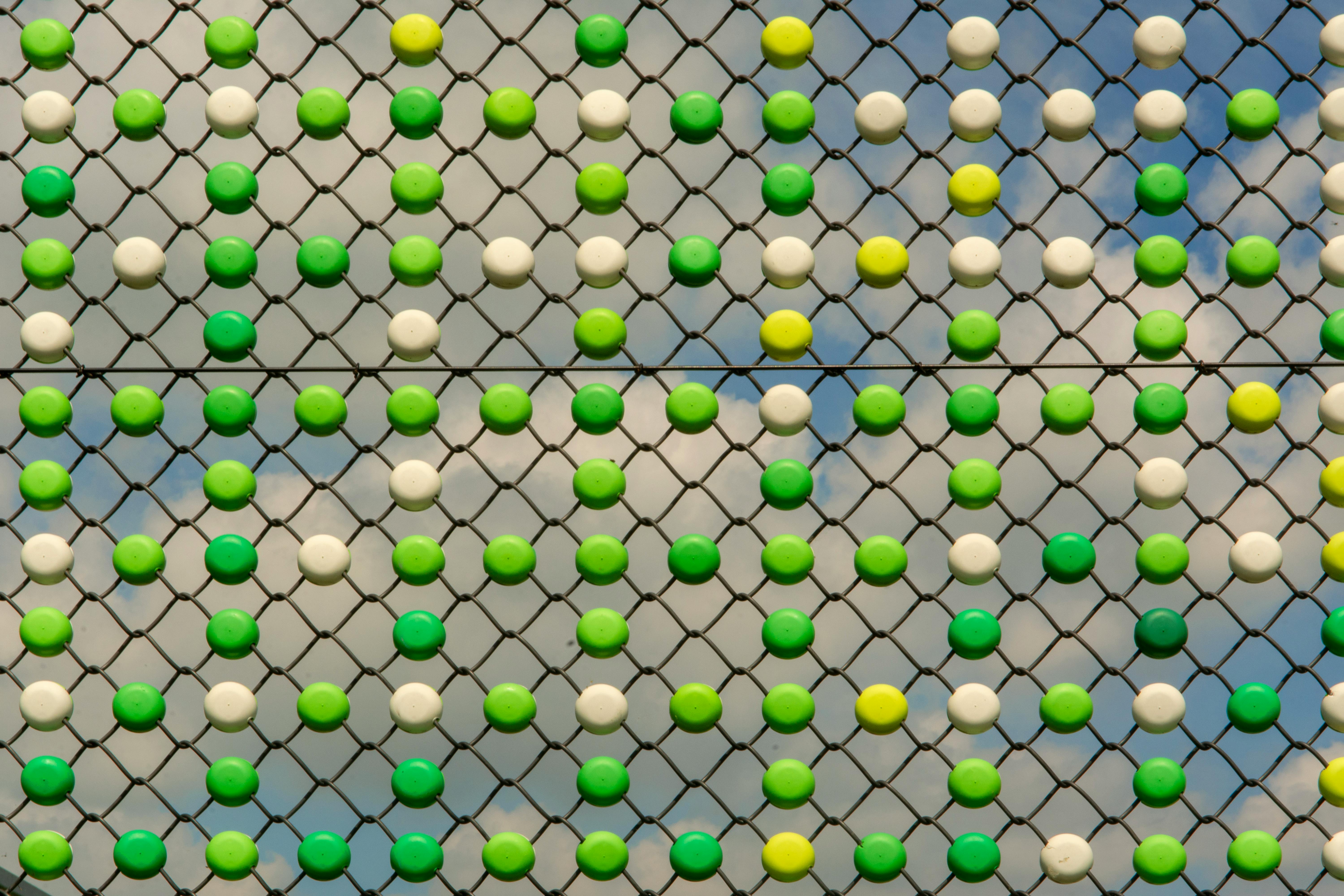 Zadarmo Svetlý geometrický vzor na plote so zelenými a bielymi kruhmi proti modrej oblohe. Fotka z fotobanky