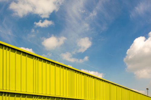 Free A vivid yellow building stands against a clear blue sky with scattered white clouds. Stock Photo