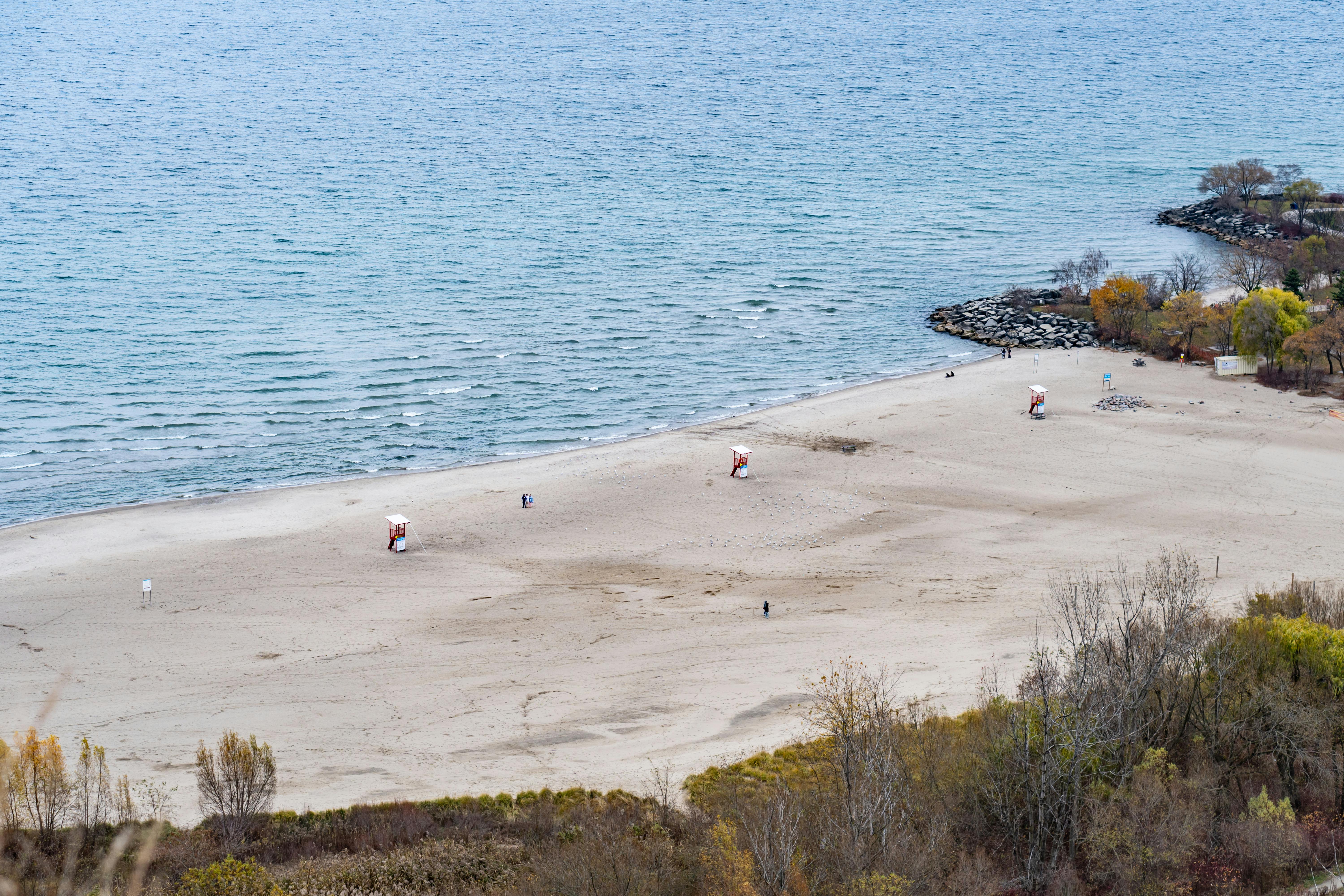 Aerial shot of a deserted beach in Toronto with lifeguard stations and colorful fall foliage.