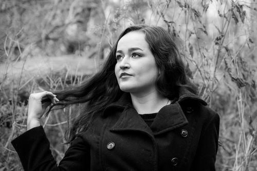 Free Black and white portrait of a woman in a forest wearing a black coat, looking thoughtful. Stock Photo