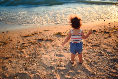Free A toddler enjoying a beach outing at sunset with flowing waves and sandy shore. Stock Photo