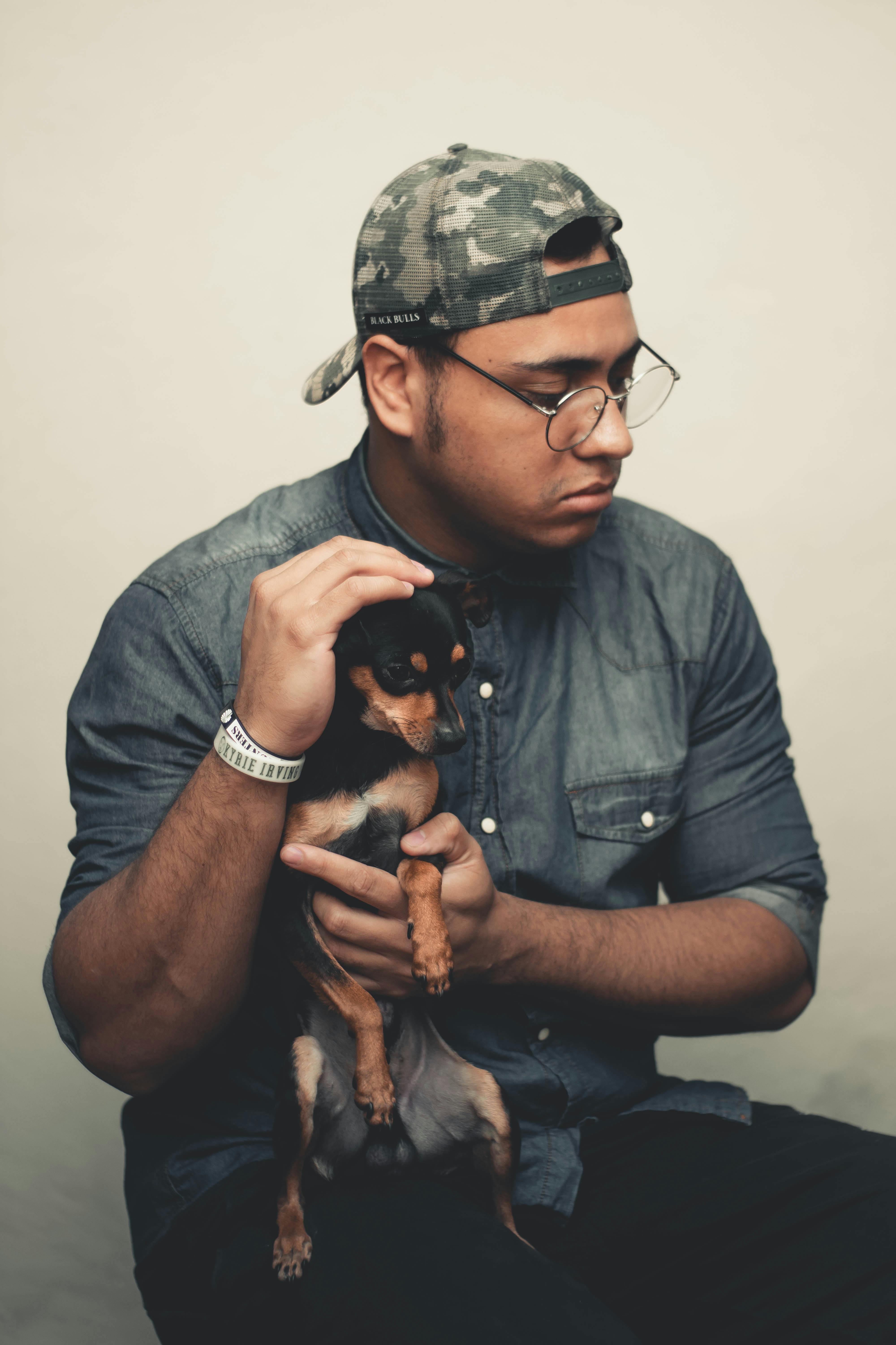 一名穿着休闲装的男子坐在室内，抱着一只黑色吉娃娃，两人之间洋溢着温暖的互动