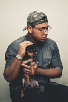 一名穿着休闲装的男子坐在室内，抱着一只黑色吉娃娃，两人之间洋溢着温暖的互动