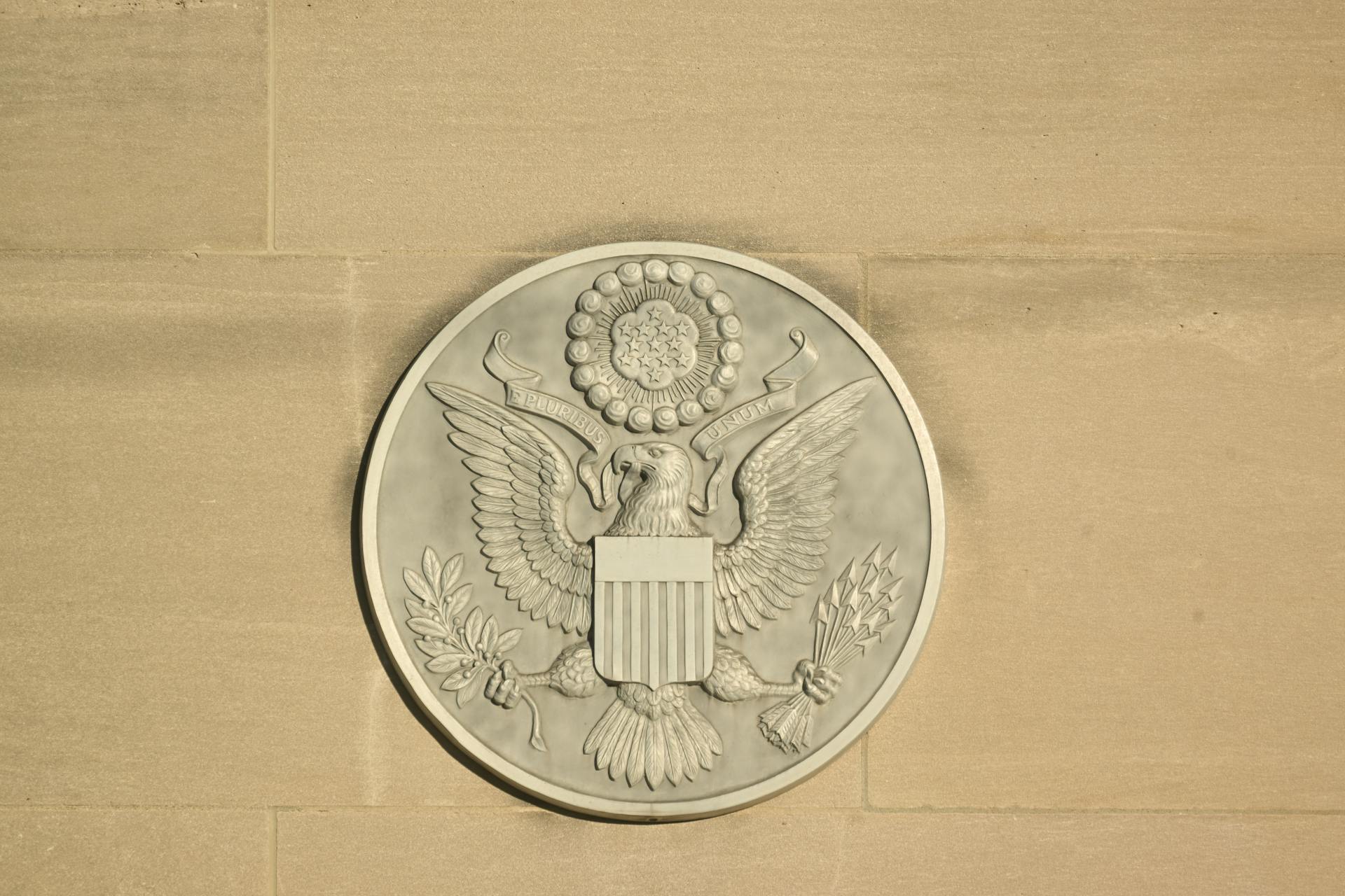 Stone carving of the Great Seal of the United States on a wall displaying an eagle with shield and olive branch.