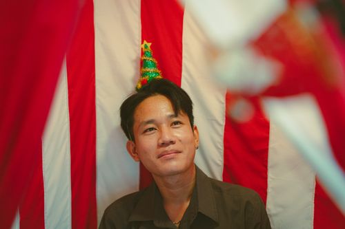 Free A person wearing a Christmas tree hat against a red and white striped background in Ho Chi Minh City. Stock Photo