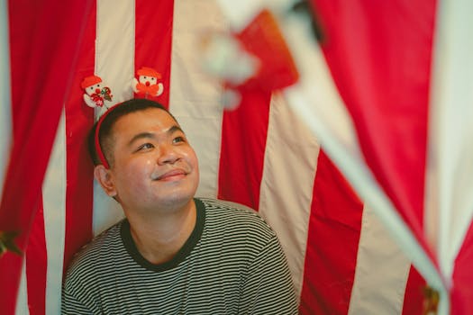 Cheerful man wearing holiday headband in a festive red and white setting.