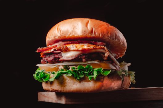 Mouthwatering grilled burger with bacon, cheese, and fresh lettuce on a rustic wooden board.