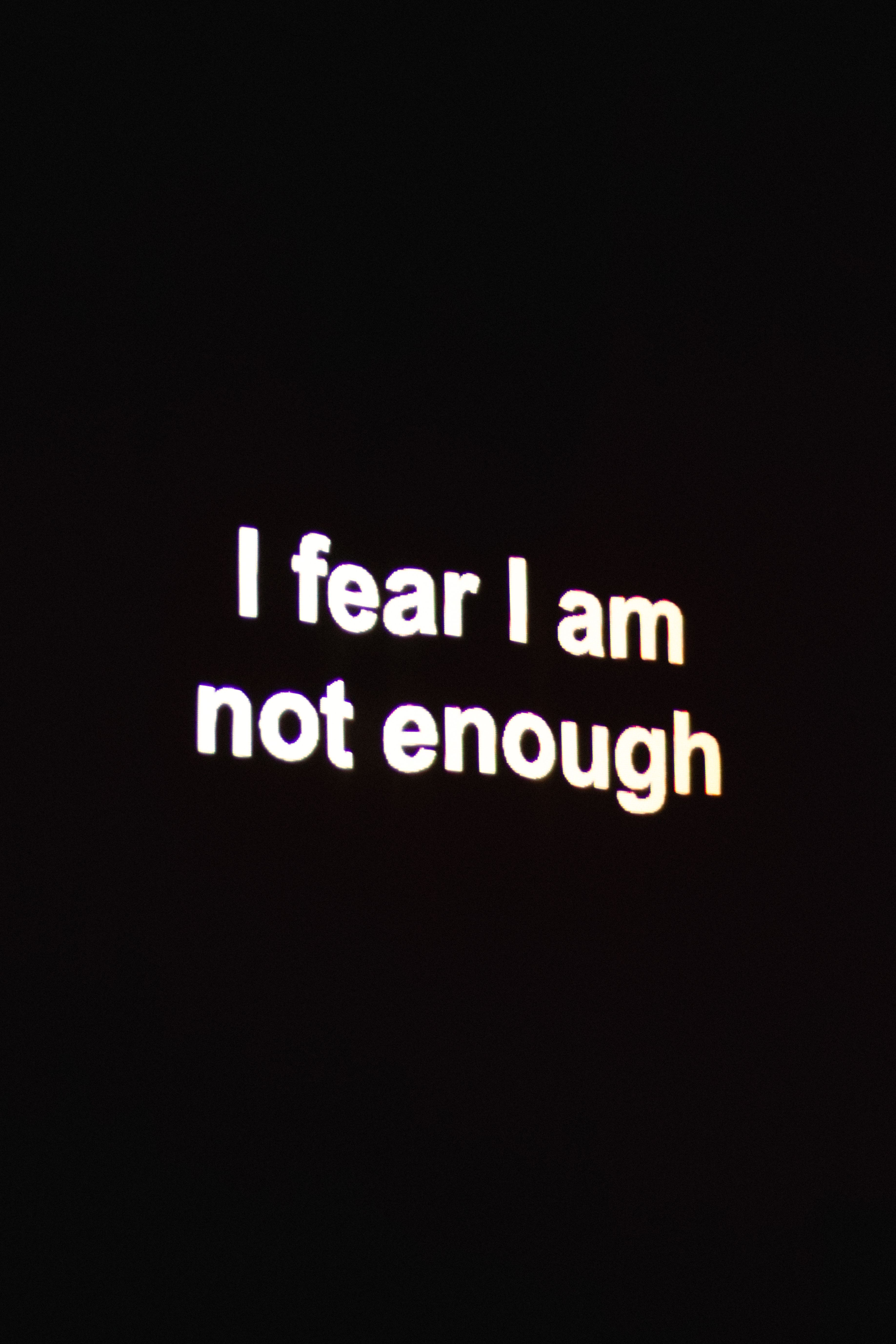 Bold typographic artwork with neon phrase 'I fear I am not enough' on a dark background.