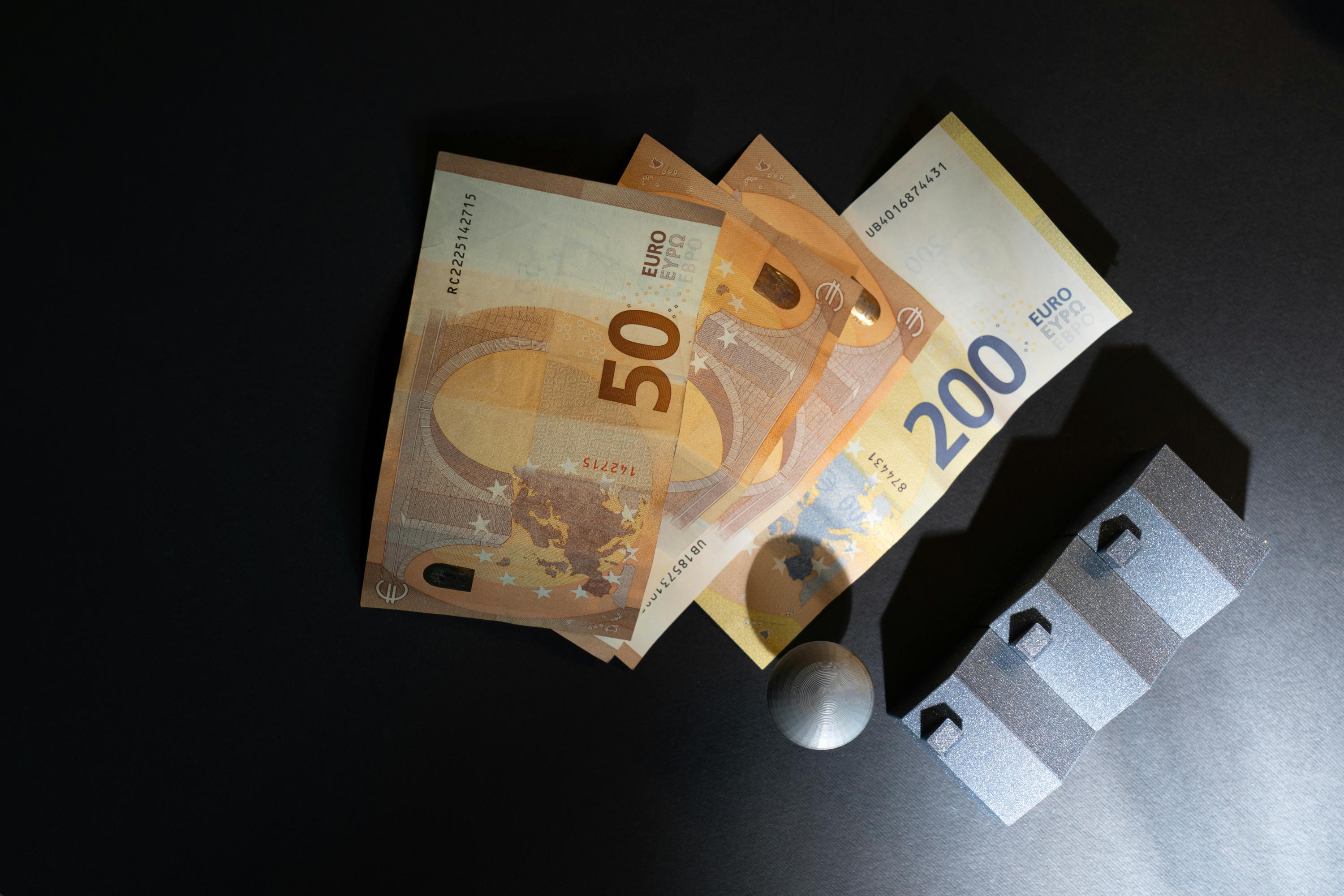 euro banknotes with silver model houses on dark surface