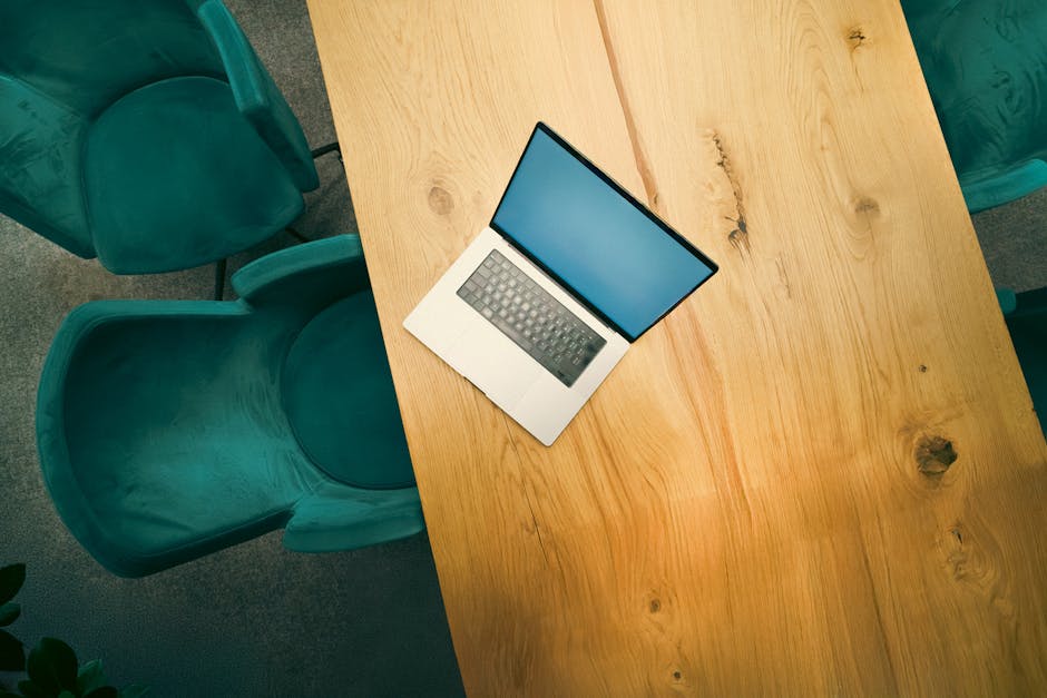 Aerial view of a laptop on a wooden table surrounded by stylish chairs in a modern office.