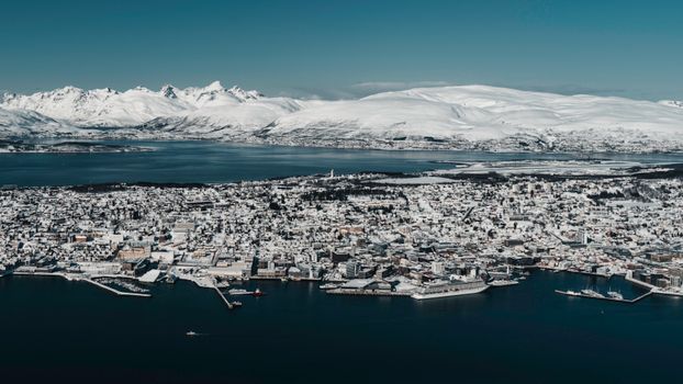 Captivating aerial view of Tromsø covered in snow, surrounded by fjords and mountains.