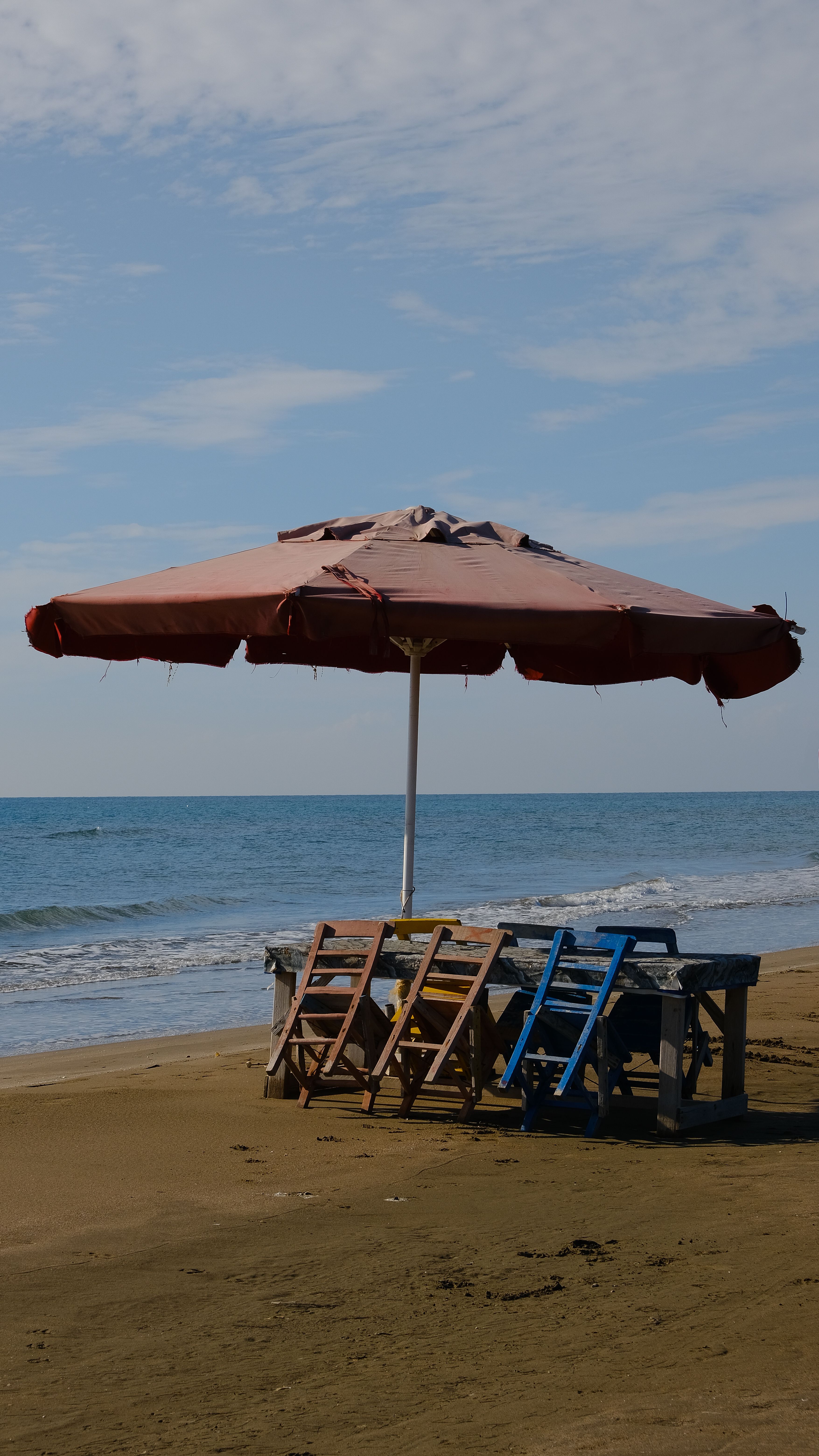 Chairs under an umbrella on a sandy beach with a calm sea view.