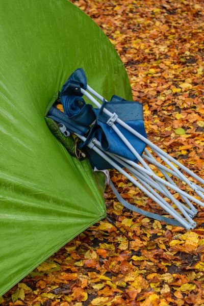 Folded camp chair in its bag beside a green tent — photo by Berna on Pexels